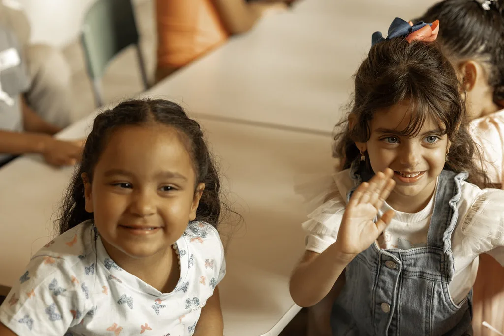 Duas crianças acenando e sorrindo durante a atividade nas mesas do Haja Kids