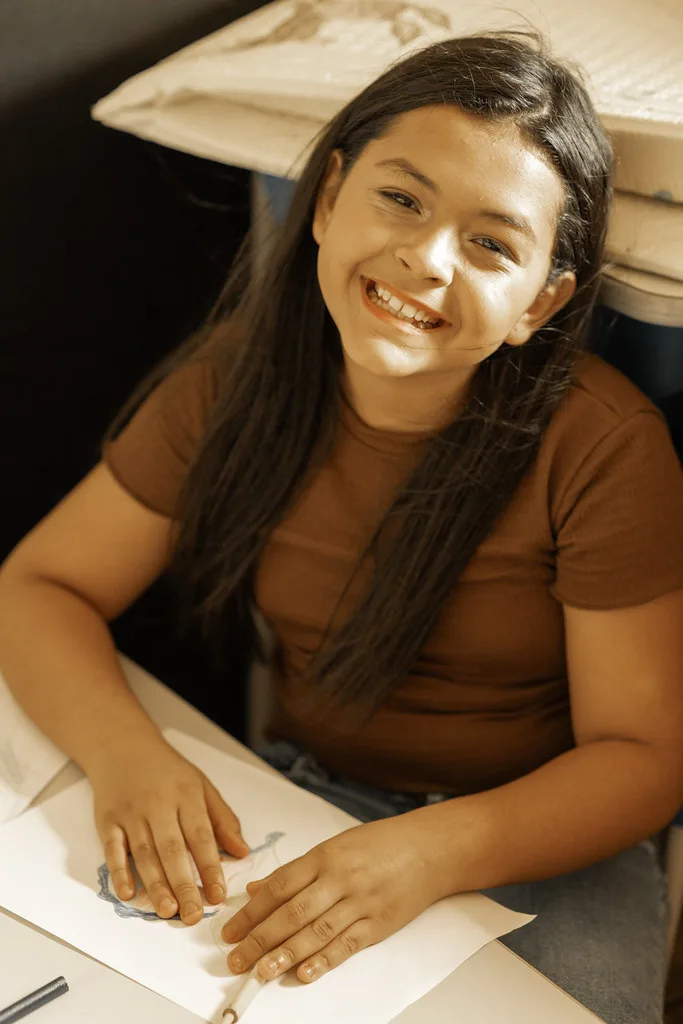 Criança sorrindo enquanto faz a atividade de desenho na mesa do Haja Kids